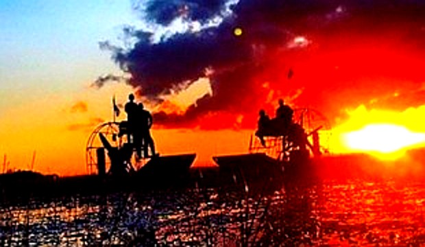 Airboats silhouetted against a vibrant Everglades sunset with golden sky and reflections on the water