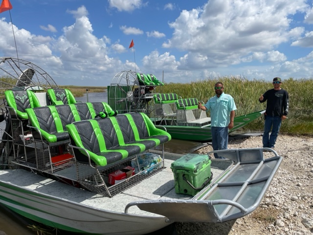 Two Everglades airboat tour guides standing next to their boats, ready to welcome guests